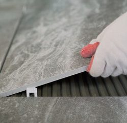 A person pouring white paint from a bucket into a paint tray on a floor.